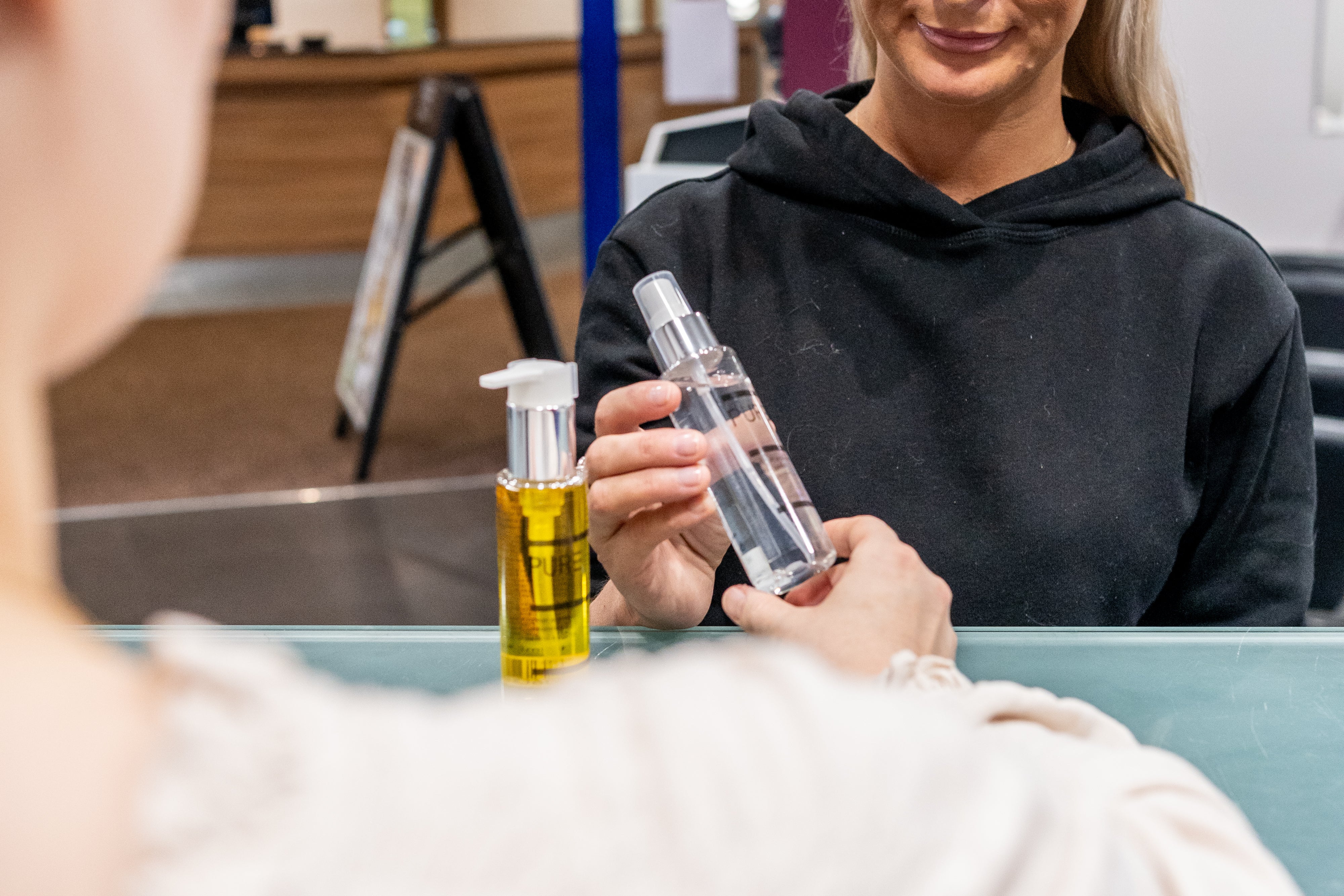 Person holding a bottle of clear liquid next to a bottle of yellow liquid, with a blurred background.